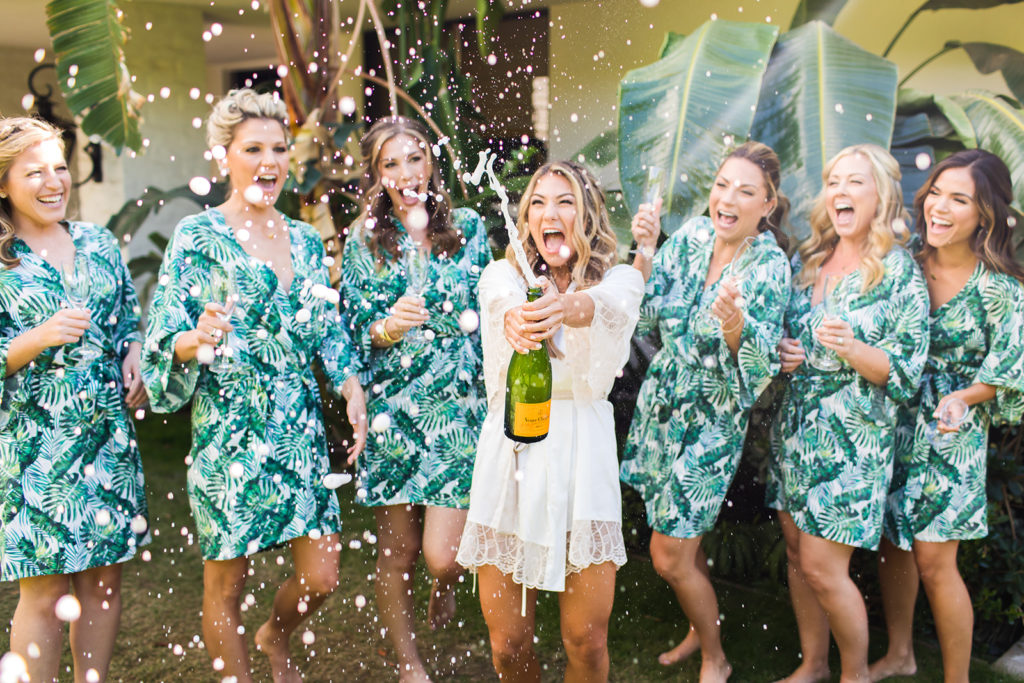bride pops champagne bottle with bridesmaids in matching robes